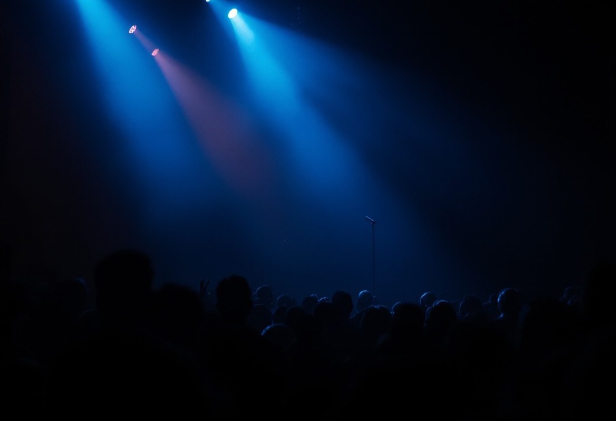 A darkened concert stage bathed in blue and amber light, two figures at microphones before a modest but attentive crowd